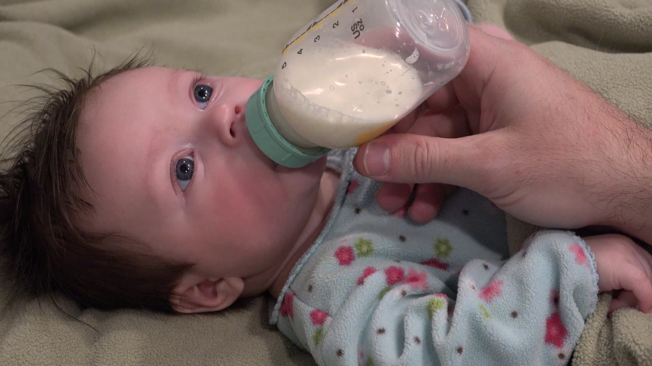 Baby drinking from bottle with adult hand near the bottle neck.