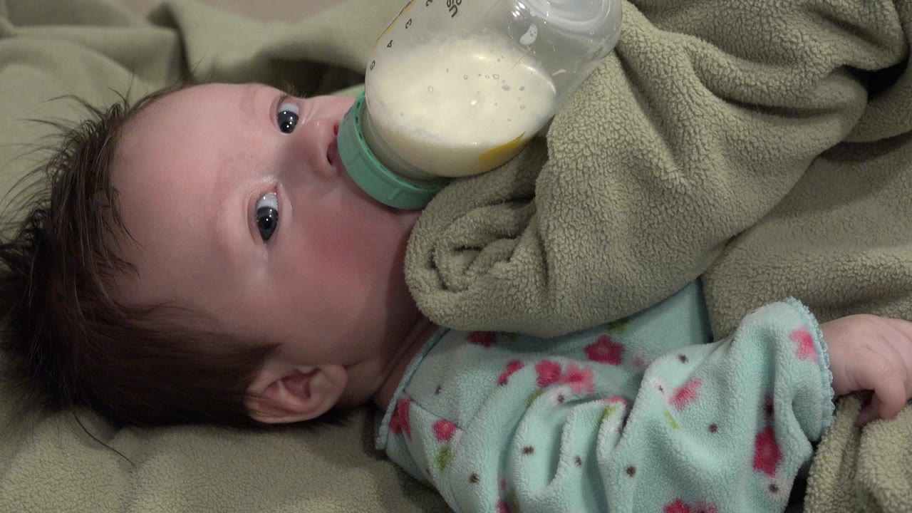 Baby lying down drinking from a bottle under a green blanket.