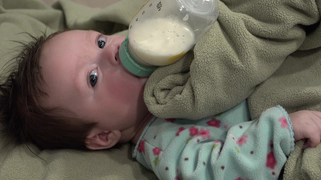 Close view of an infant bottle feeding under indoor light.