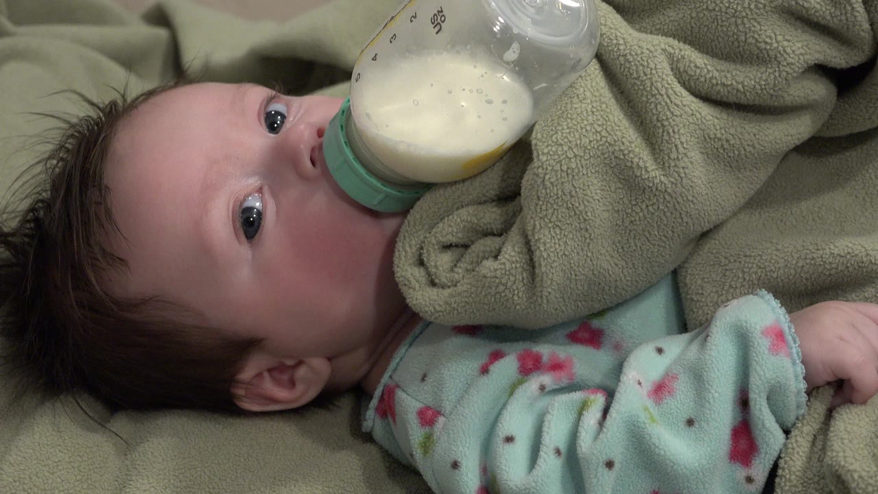 Baby drinking from a milk bottle while lying on a blanket.