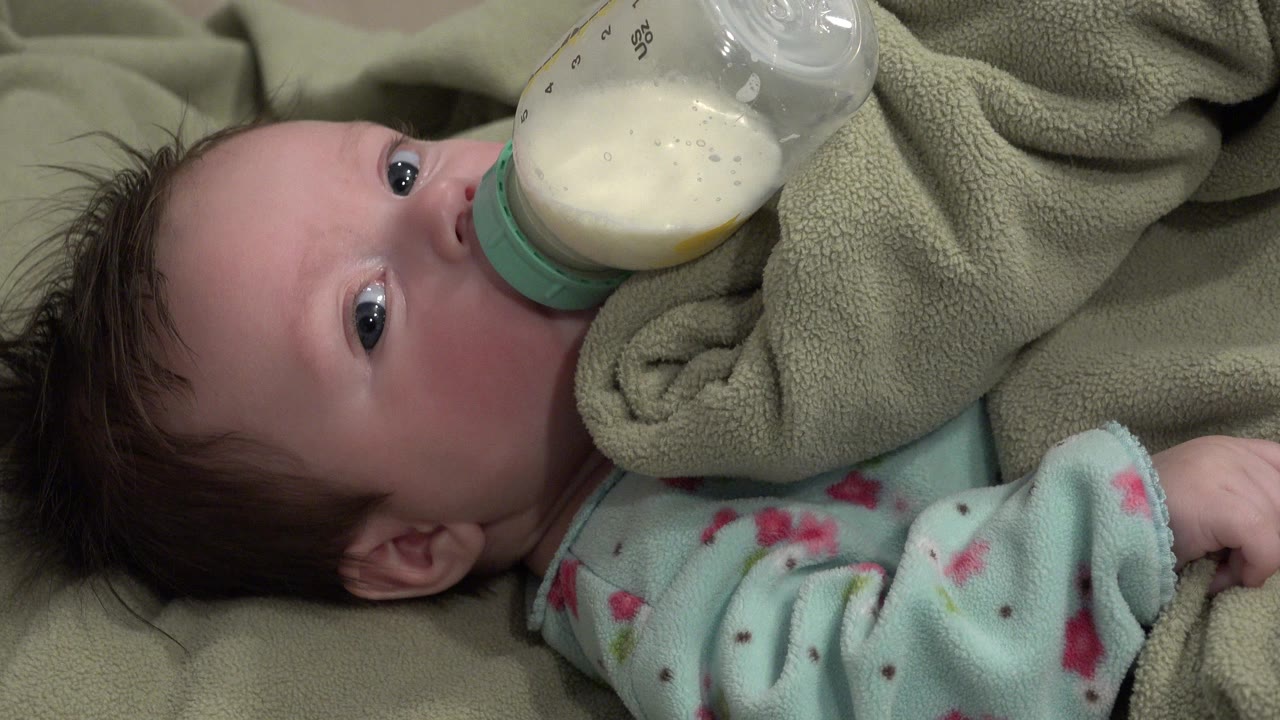Baby lying under a blanket while drinking from a bottle.