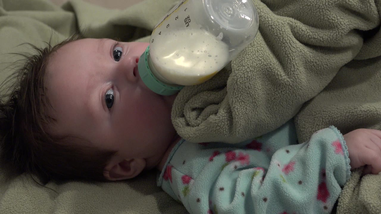 Baby lying on blankets with a milk bottle at the mouth.