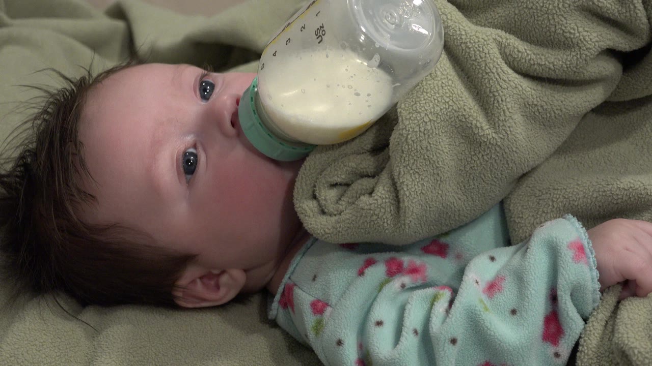 Infant lying on a blanket with a milk bottle at their mouth.