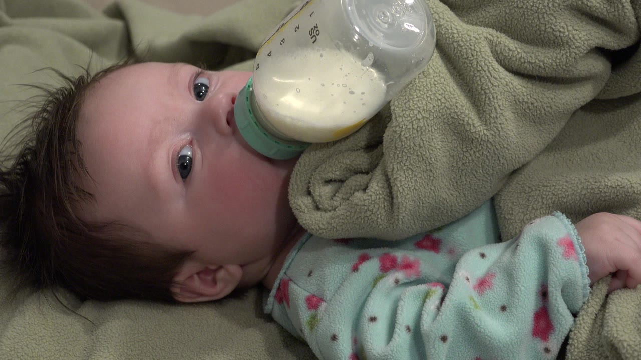 Baby lying on blankets and drinking from a milk bottle.