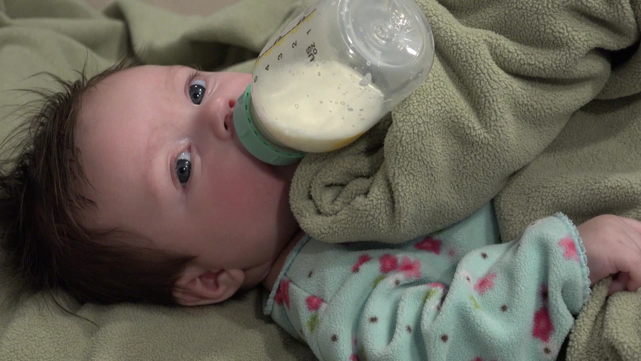 Baby lying on blankets drinking from a bottle.