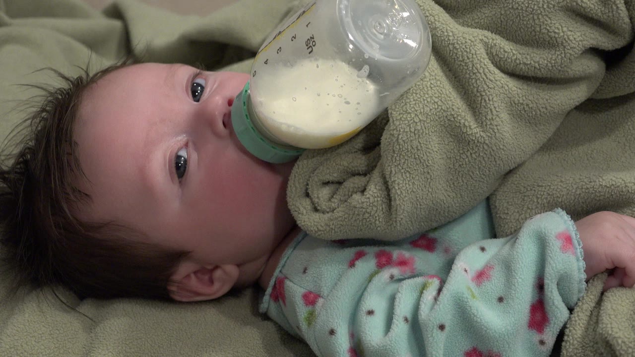 Infant lying on a green blanket drinking from a clear bottle.