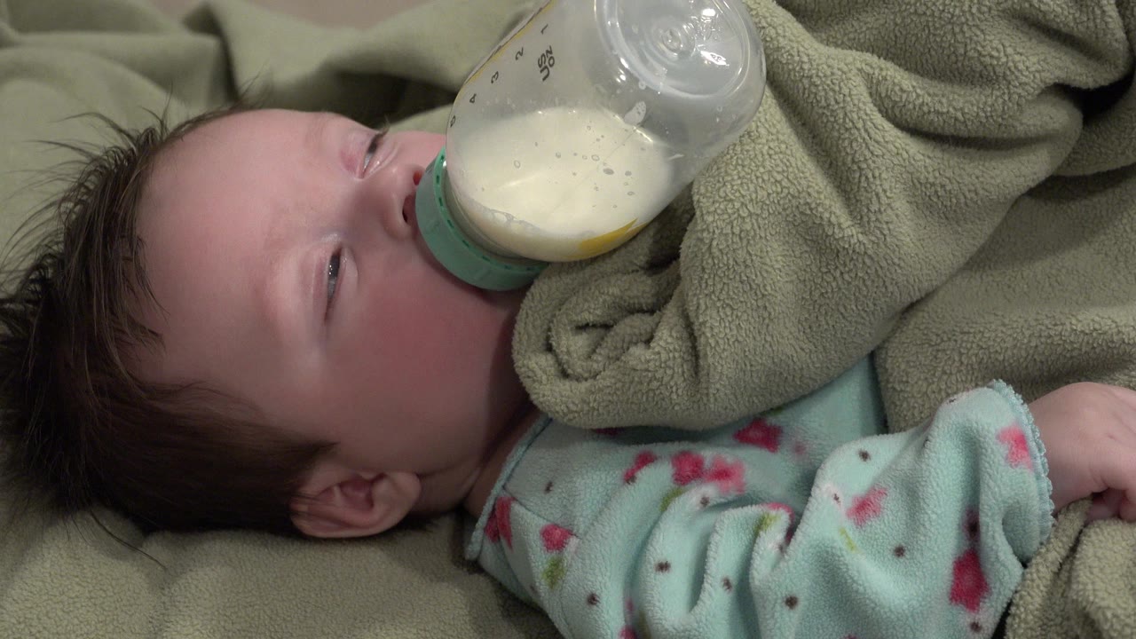 Baby drinking from a bottle while lying under a blanket.