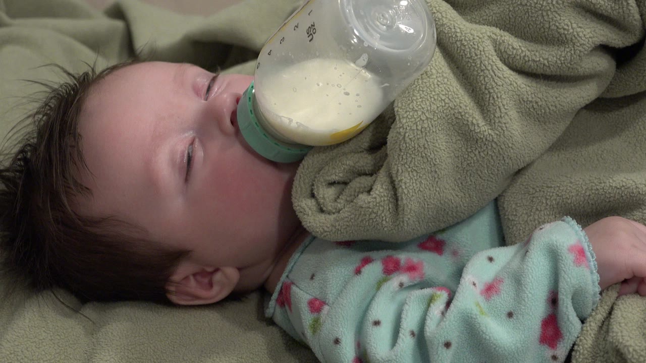 At 0:01 in Westminster, Colorado, the baby remains tucked in fleece with the bottle angled down toward the mouth and the eyelids mostly shut.