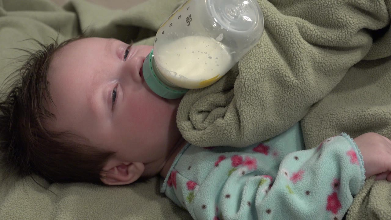 At 0:02 in Westminster, Colorado, the baby's eye is slightly more open as the milk bottle covers part of the face and the fleece blanket bunches near the cheek.