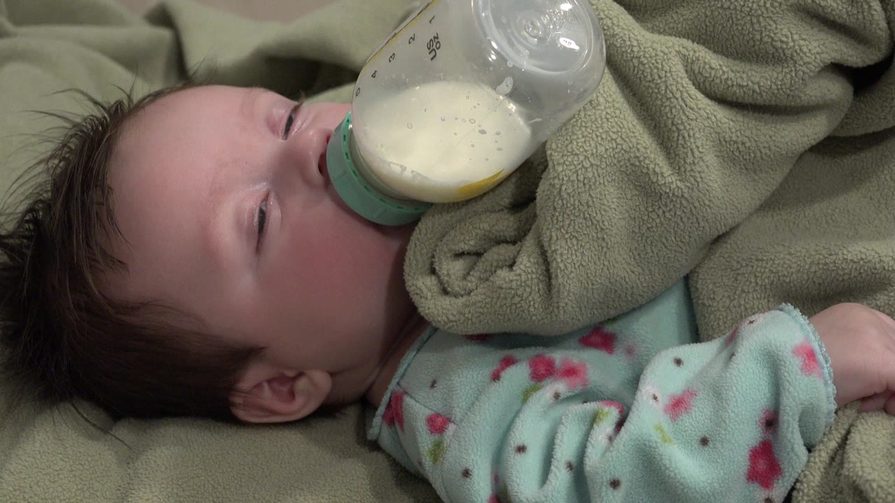 Close view of a baby drinking milk from a bottle on blankets.
