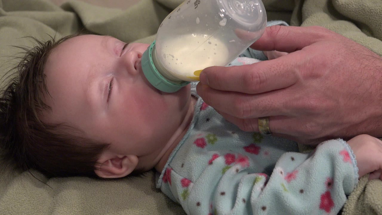 Baby drinking from a bottle while lying on a blanket.
