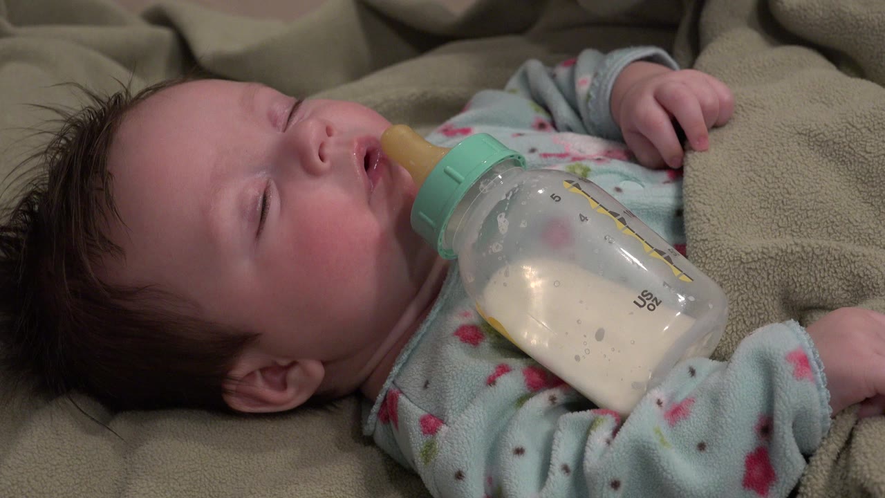 Infant lying on a green blanket with a bottle at the mouth.