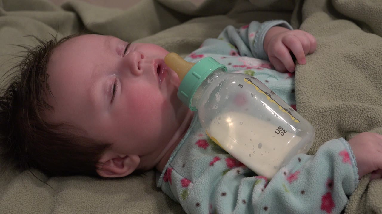 Sleeping baby beside a milk bottle on a beige blanket.