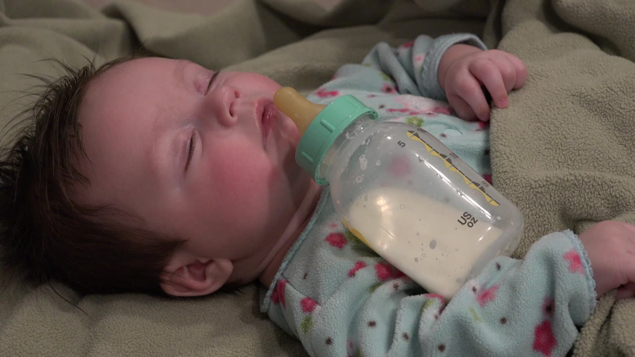 Sleeping baby with a milk bottle on beige fabric.