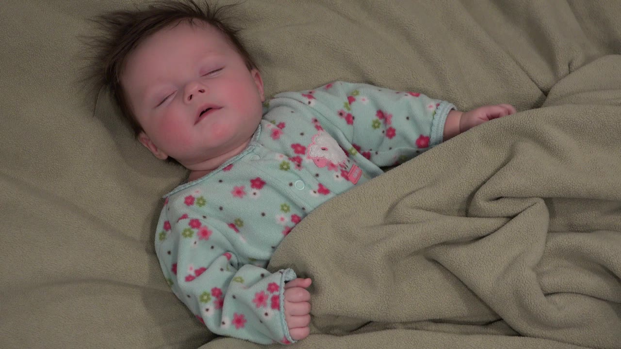 Sleeping baby in floral pajamas under a tan blanket.