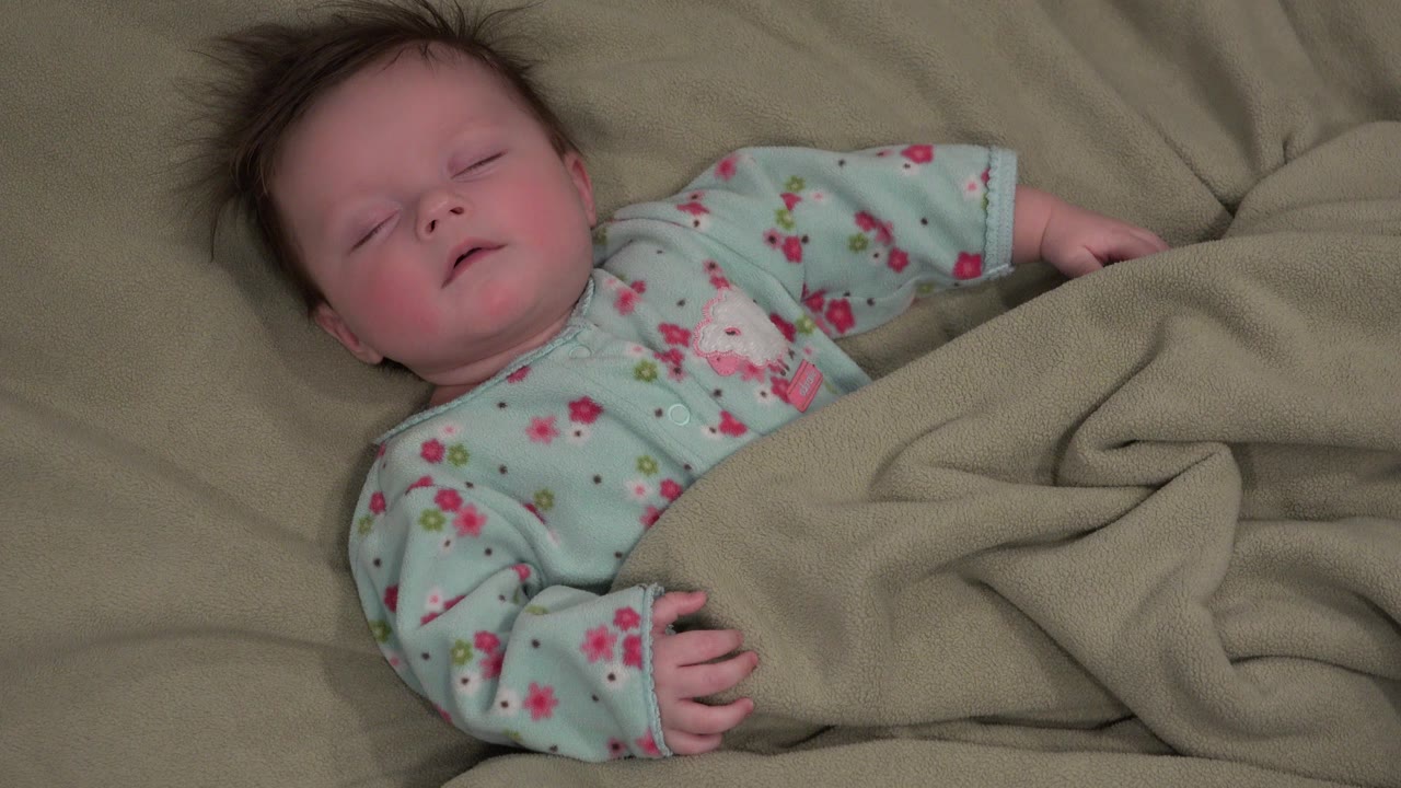Sleeping baby on a bed under a tan blanket.