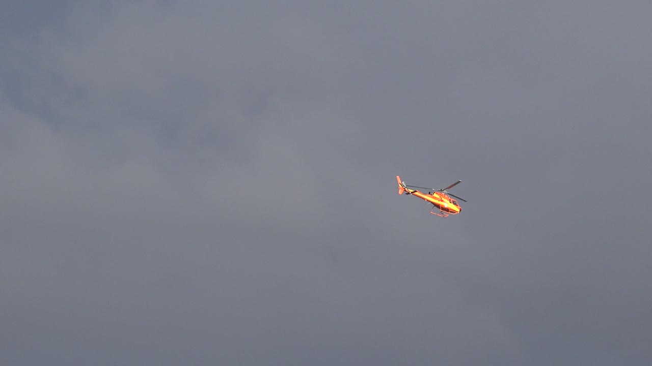 Distant sunlit helicopter centered high against muted gray-blue clouds in Westminster, Colorado, with no visible people.