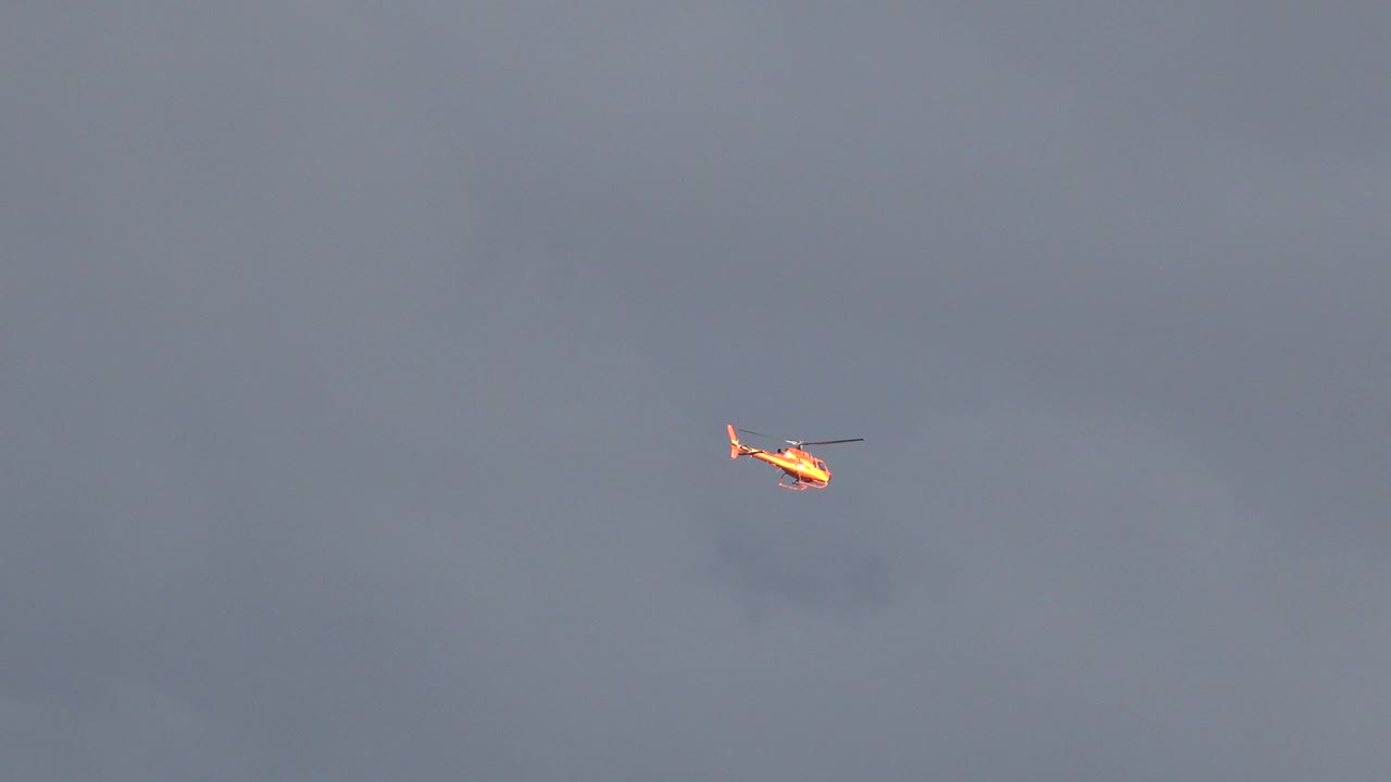 Red and white helicopter held near the upper center of the Westminster, Colorado frame with soft gray cloud cover behind it and no visible people.