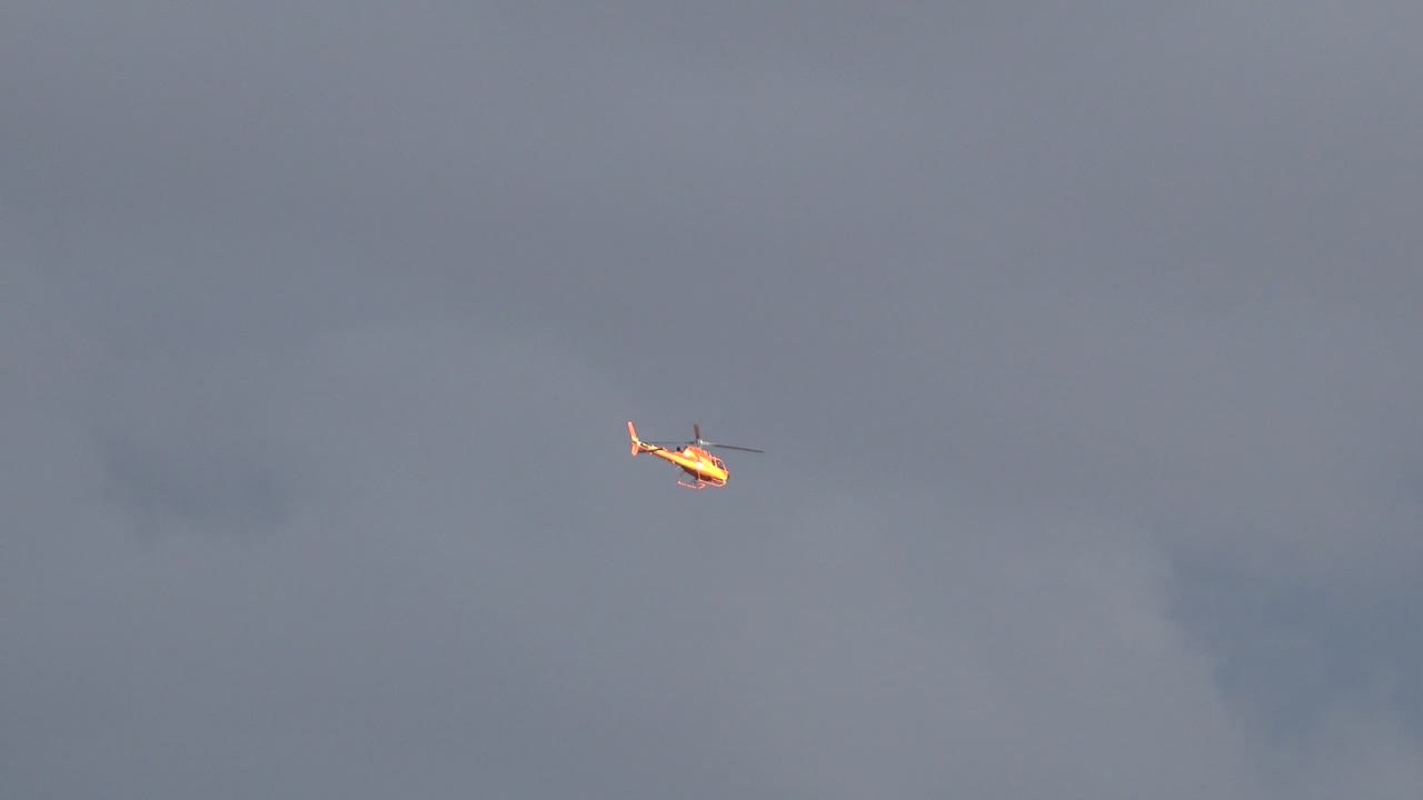 Small helicopter flying below darker cloud patches.