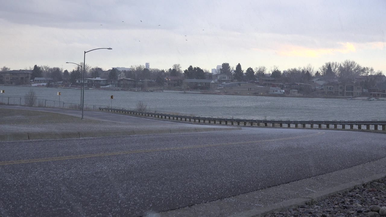 Heavy hail over wet asphalt with a streetlight and fenced water behind