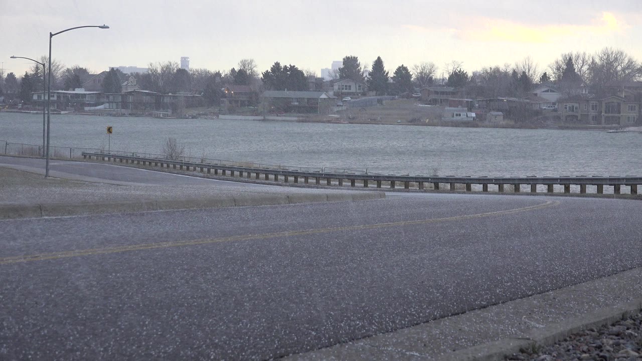Wet road beside a lake with guardrail and distant houses.