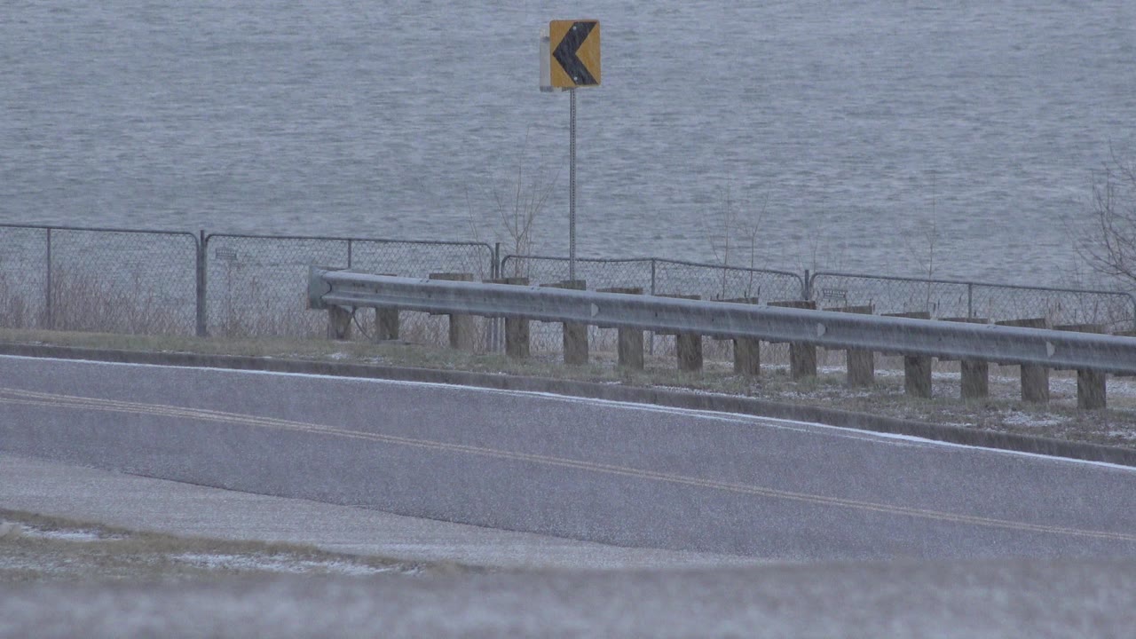 At 0:01 in Westminster, Colorado, the same wet bridge-side road stays empty under rain, with the chevron sign centered above the guardrail and no visible people.