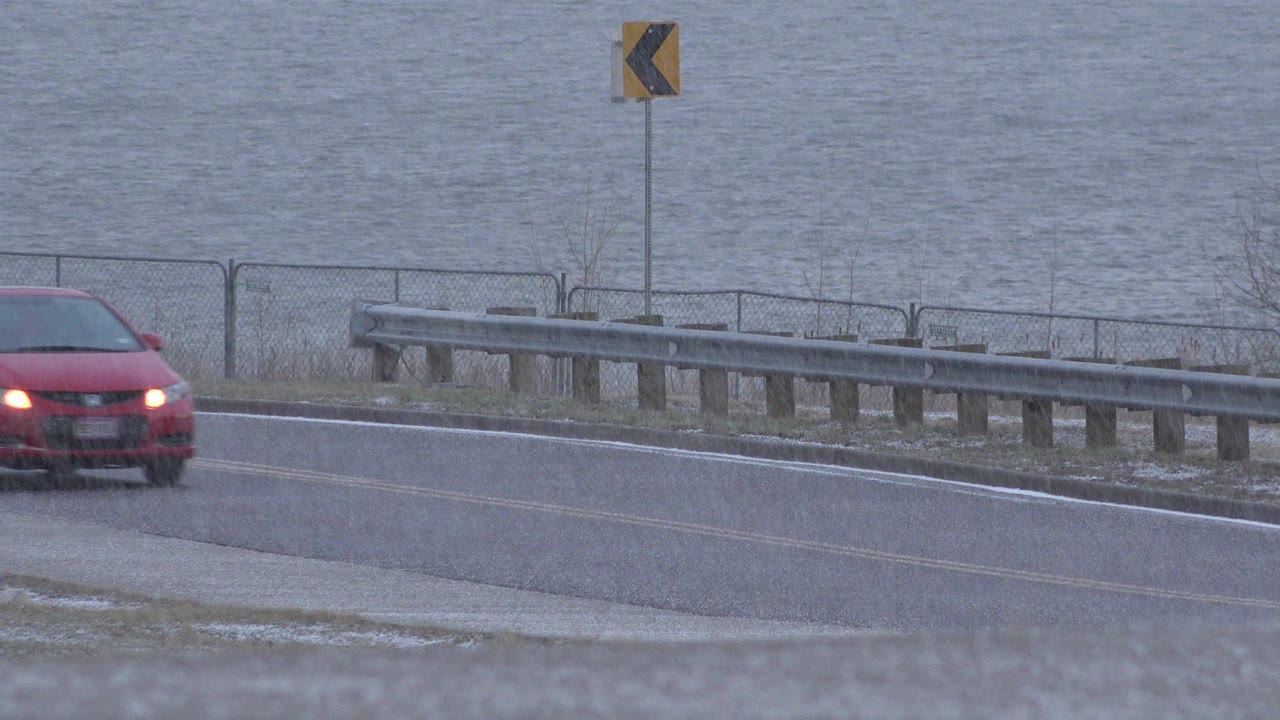 Red car partly entering a roadside frame beside water.