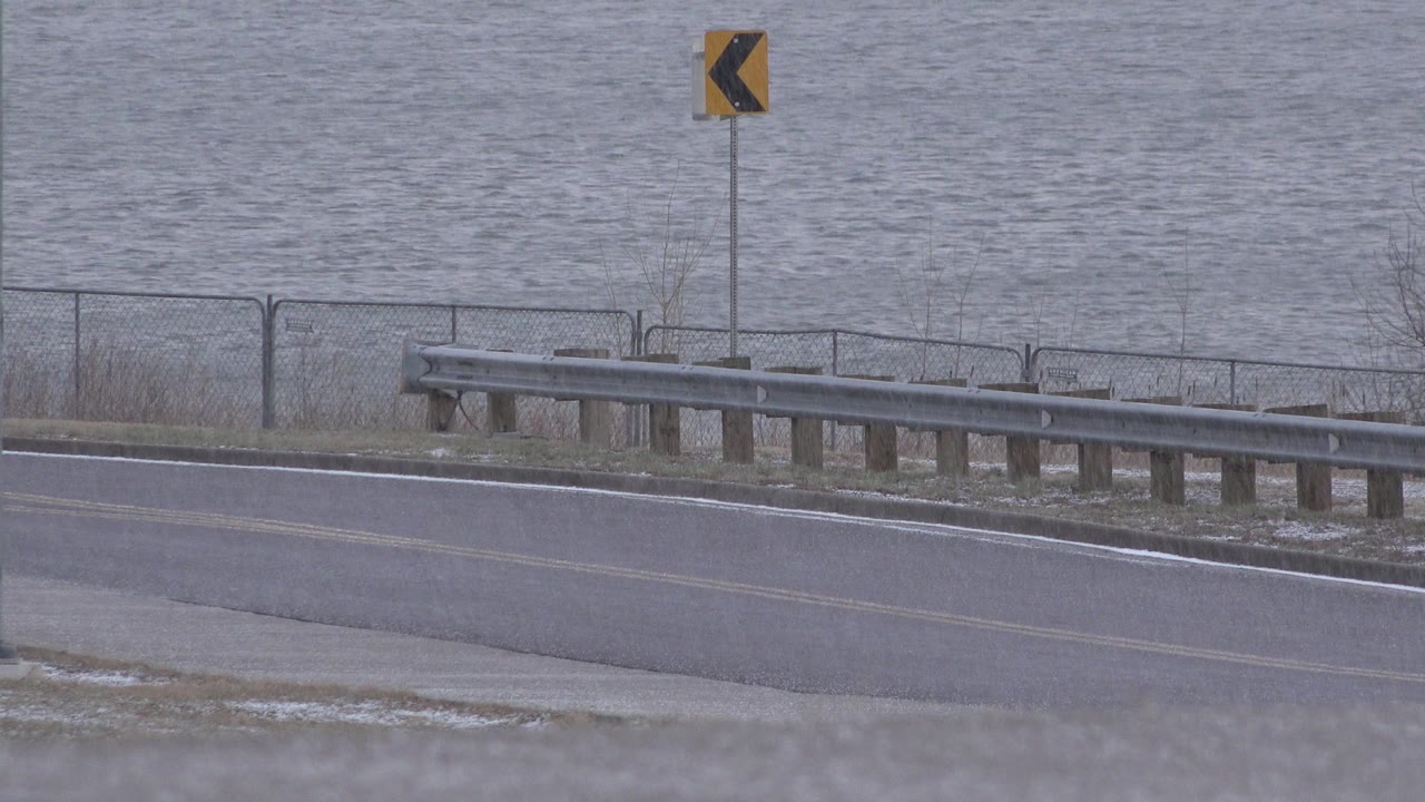 Quiet road edge, guardrail, fence, and gray water.