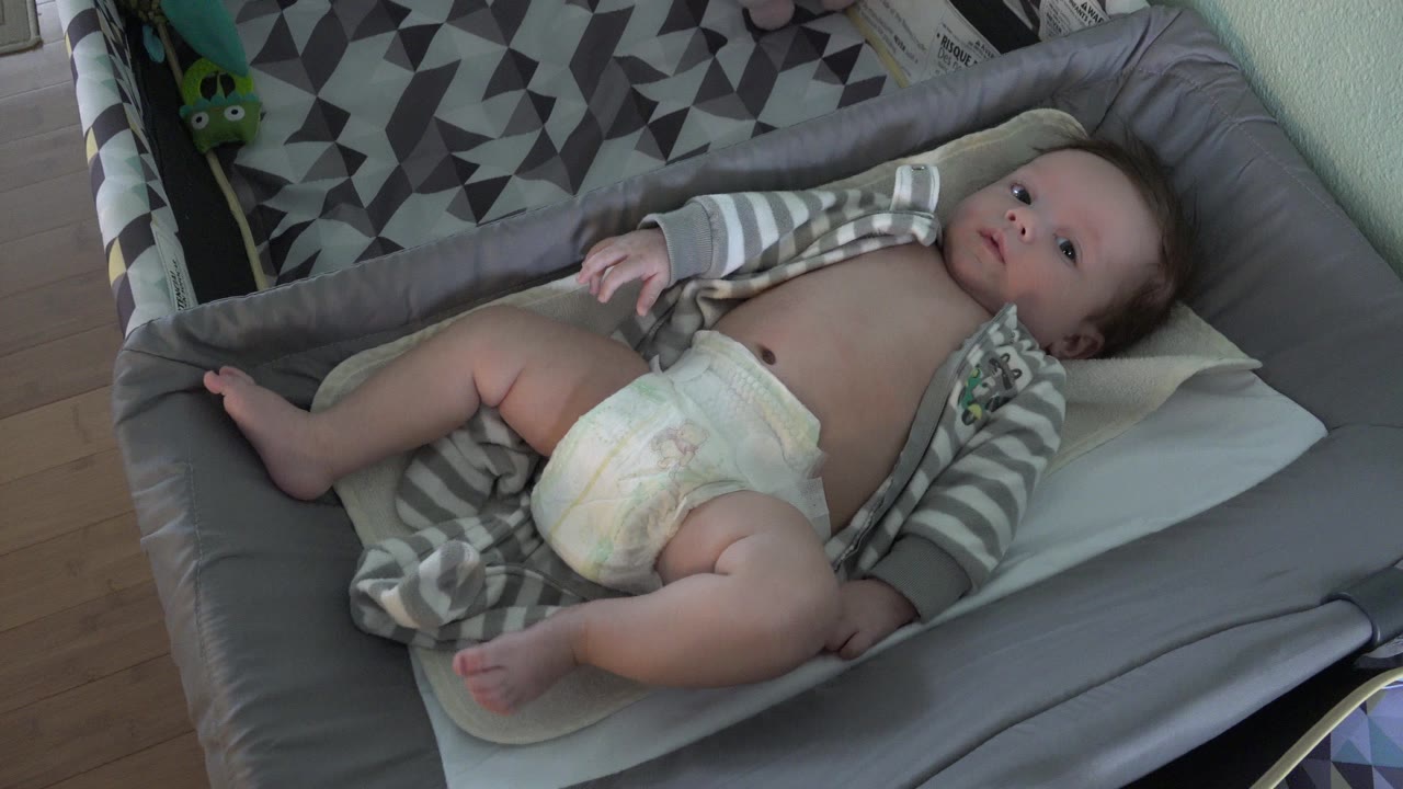 Baby lying on a gray changing pad in a home interior.