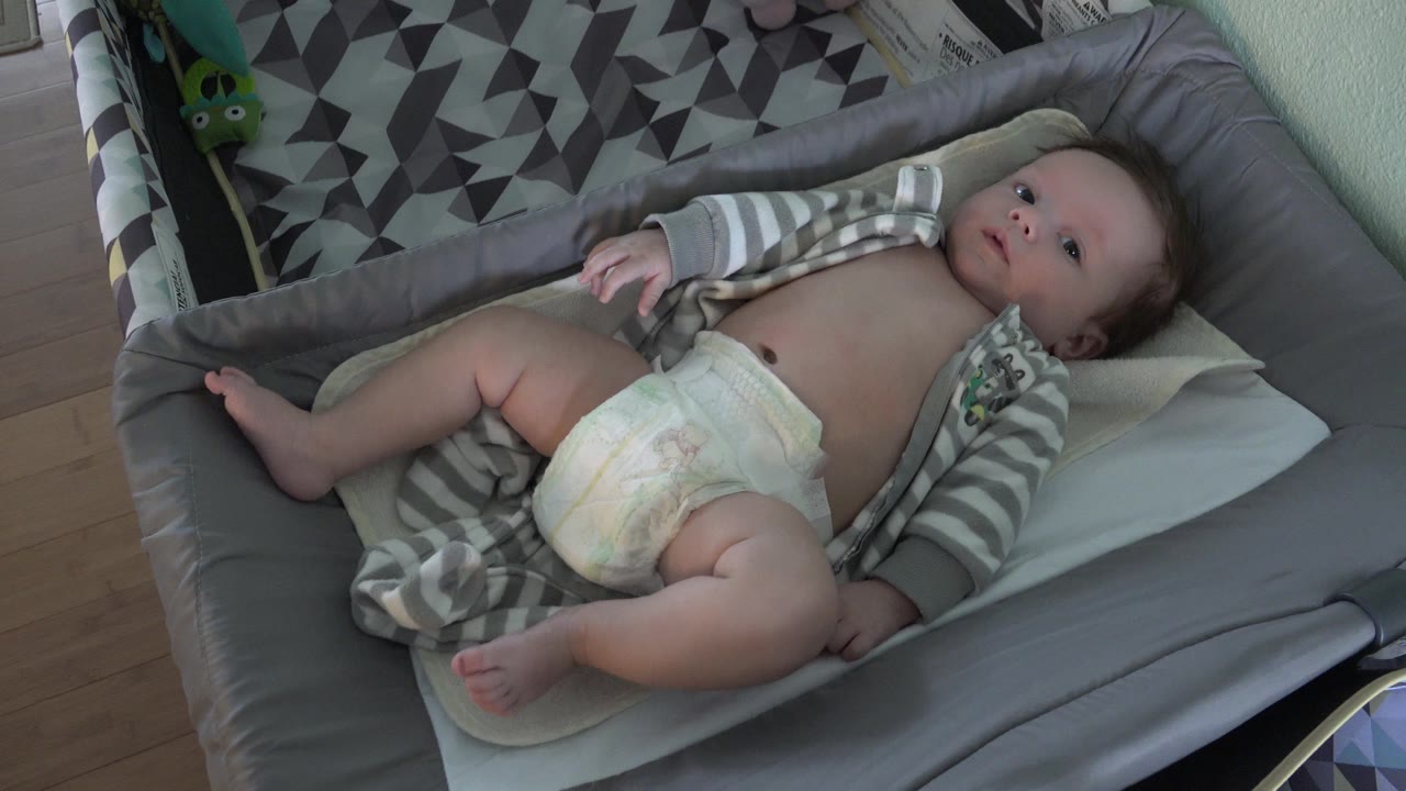 One second into the Westminster, Colorado footage, the baby looks upward from the changing pad while the diapered legs rest near the left side of the frame.