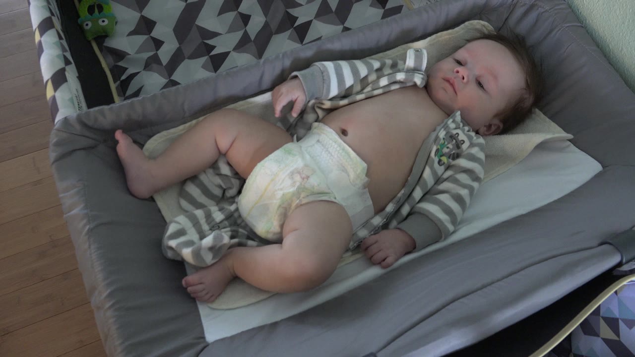 Baby lying on a tan pad in a gray cushioned seat.