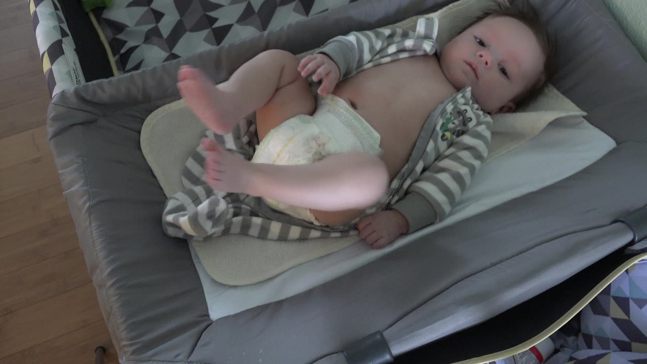The infant remains centered on the padded changing surface as both legs lift higher toward the camera in the Westminster home interior.