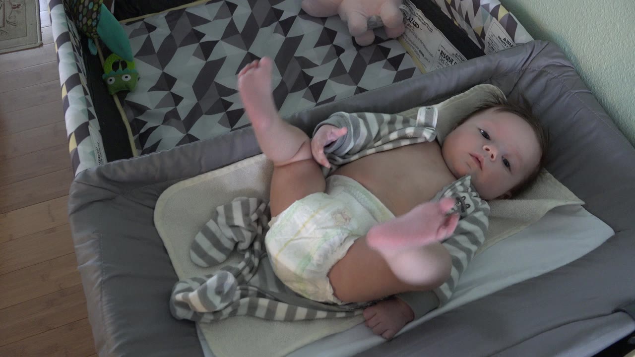 Baby lying in a gray bassinet with legs raised.
