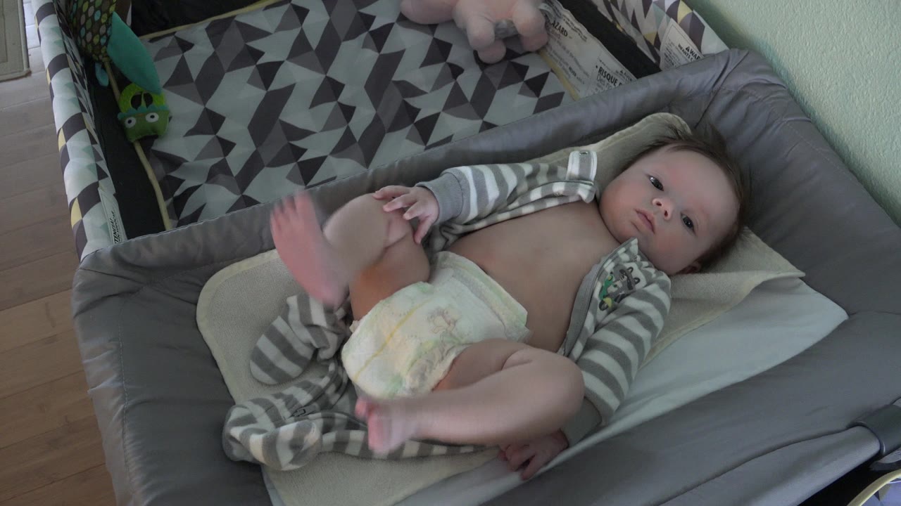 Baby lying in a gray bassinet with legs raised.