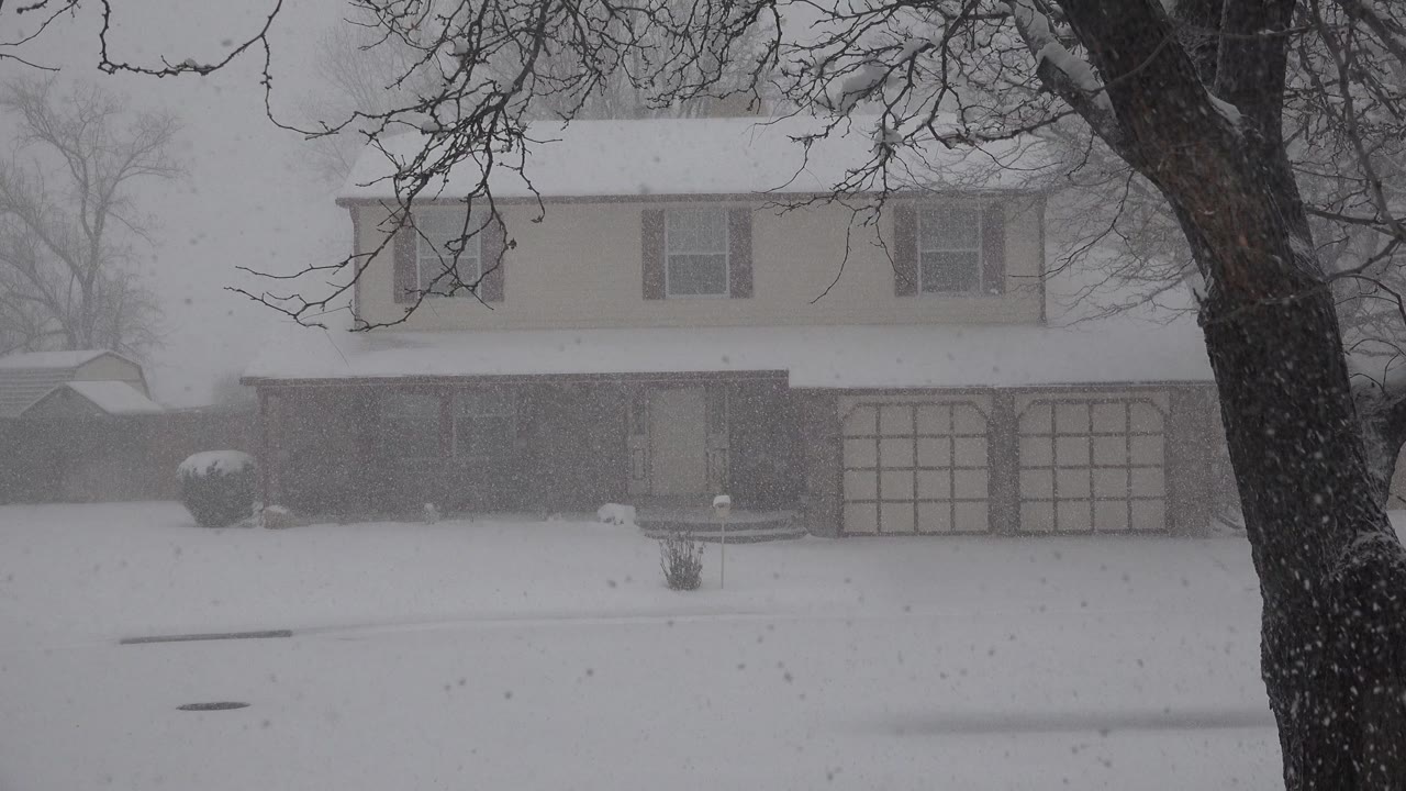 At 0:01, the same Westminster, Colorado home remains centered behind the snow-covered lawn, with garage doors visible through blowing snow and no visible people.