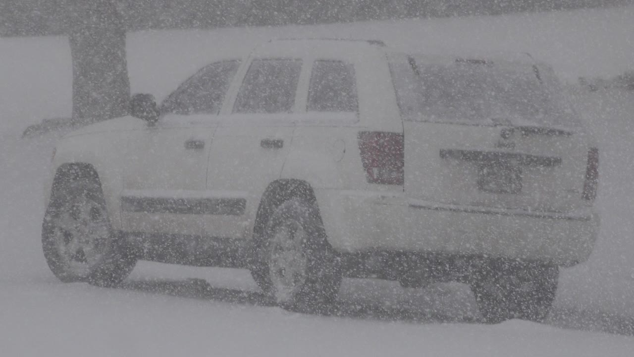 White SUV seen from the rear passenger side in heavy snow in Westminster, Colorado, with the lot and background mostly obscured and no visible people.