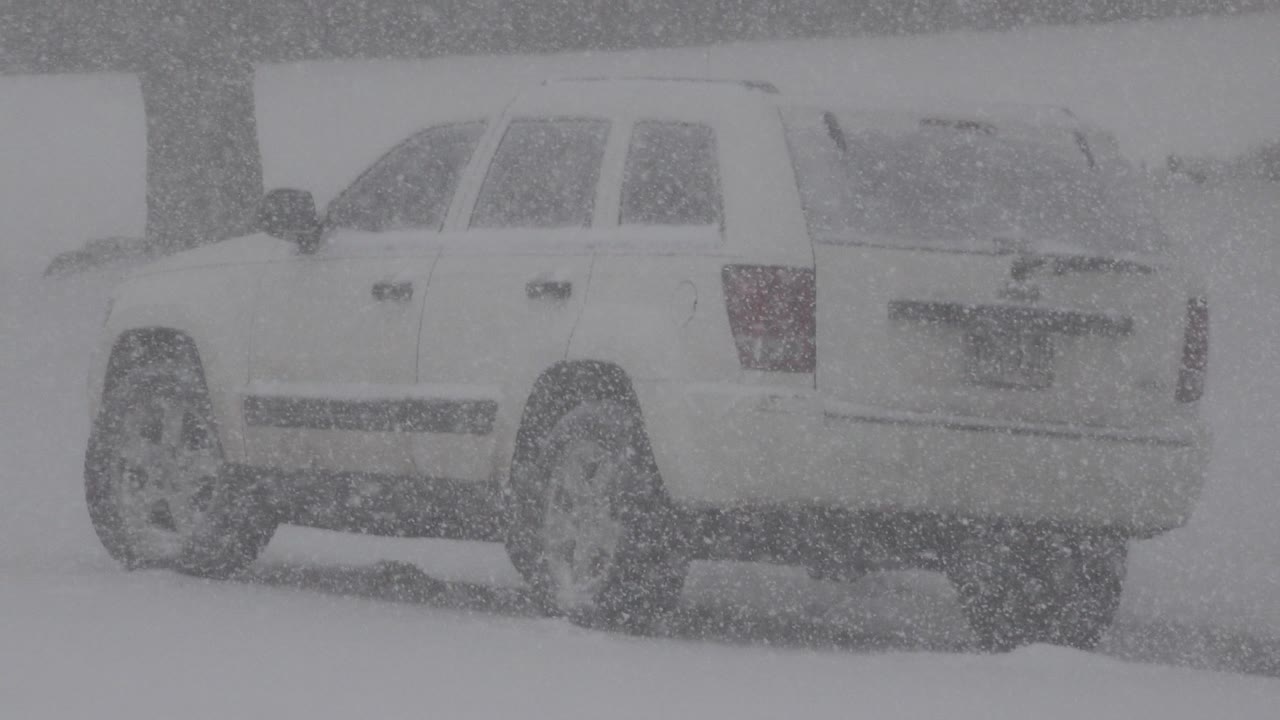 Parked white SUV remains centered in dense snowfall in Westminster, Colorado, with its rear hatch and side windows muted by snow and no visible people.