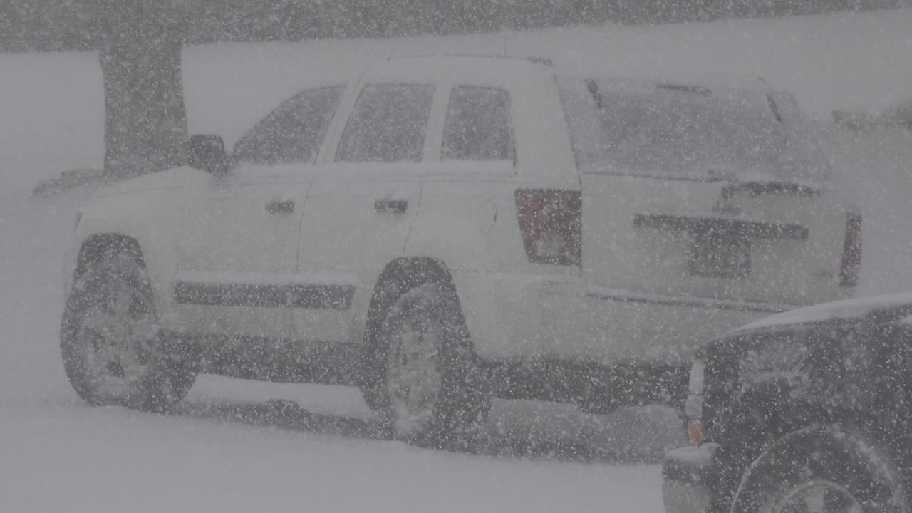 White vehicle on a snowy road during heavy snowfall.