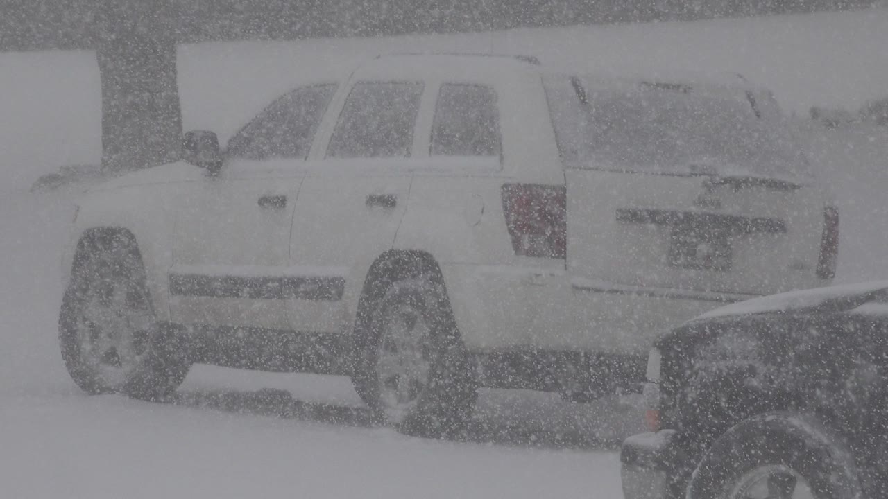 The white vehicle remains in the midground on the snowy Westminster, Colorado roadway as blowing flakes obscure the background, with no clearly visible people.