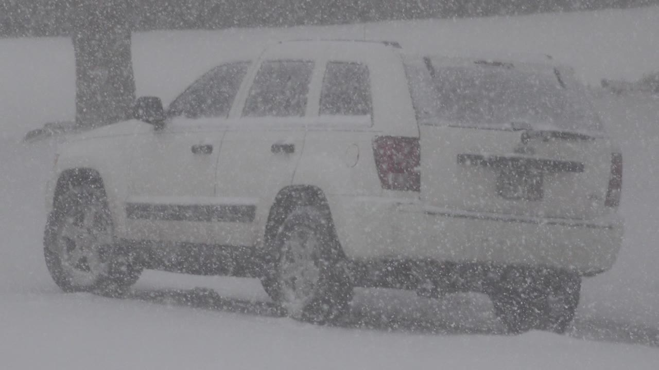 The SUV remains in a side-rear view in Westminster, Colorado, with the rear hatch and left side partly veiled by blowing snow and no visible people.