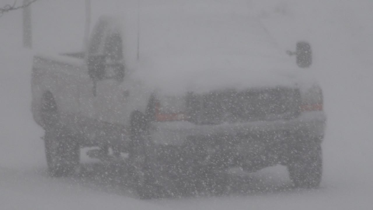 A light-colored vehicle is seen close up through heavy falling snow in Westminster, Colorado, with the front grille and side mirror faintly visible and no visible people.