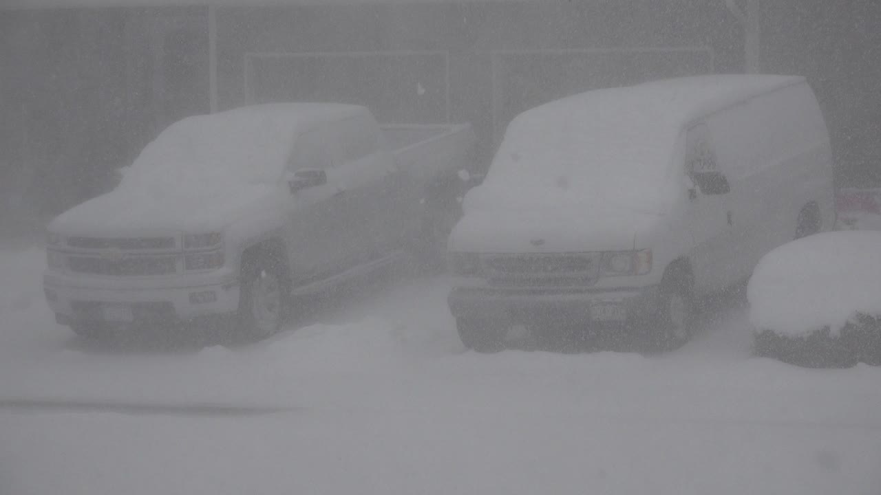 At 0:01, the pickup and van remain parked in the same snowy Westminster, Colorado residential view, with flakes reducing contrast and no visible people.