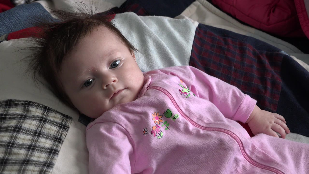 Baby girl in a pink onesie lying on pillows.