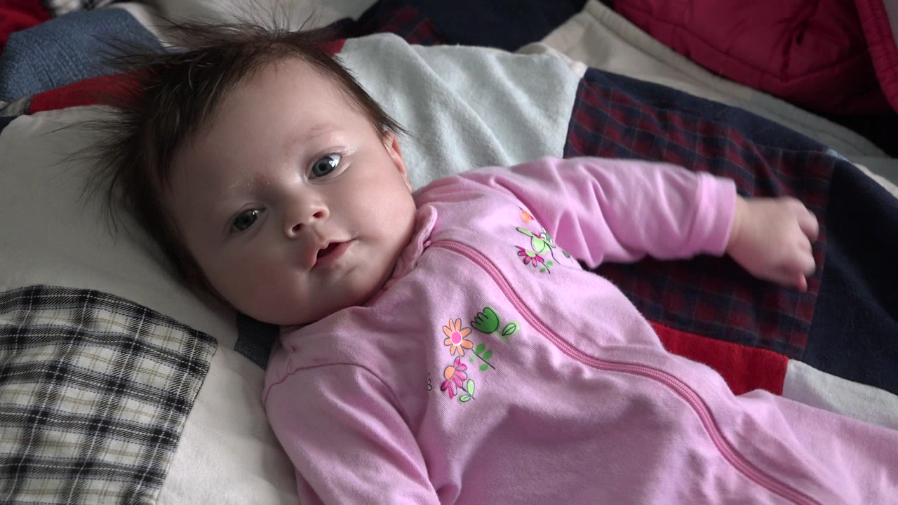 Infant in a pink sleeper lying on a patchwork quilt.