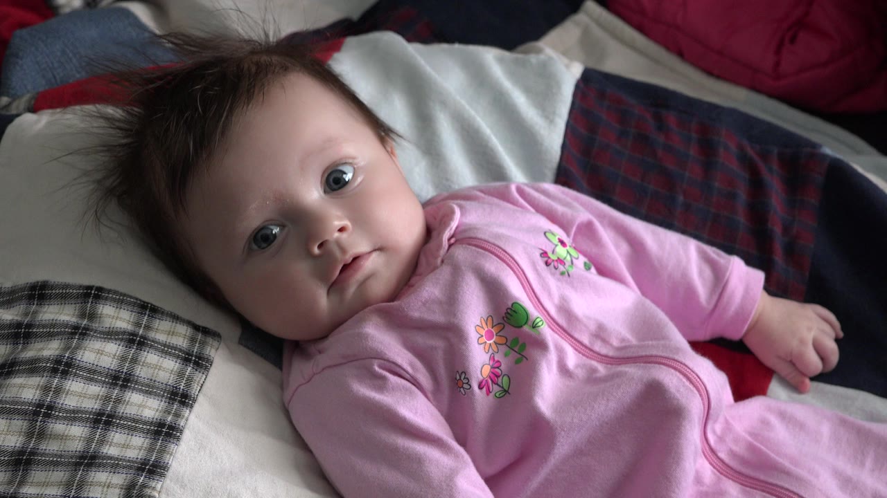Young child in a pink outfit lying on patterned bedding.