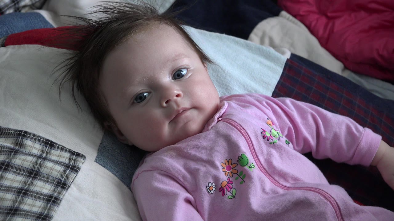 Baby in a pink outfit lying on pillows and blankets.