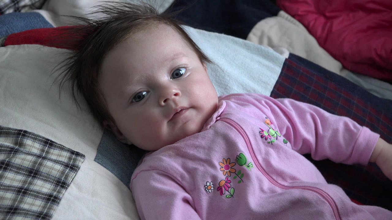 At 0:01, the baby remains reclined on pillows in Westminster, Colorado, looking forward with one arm extended toward the right edge of frame.