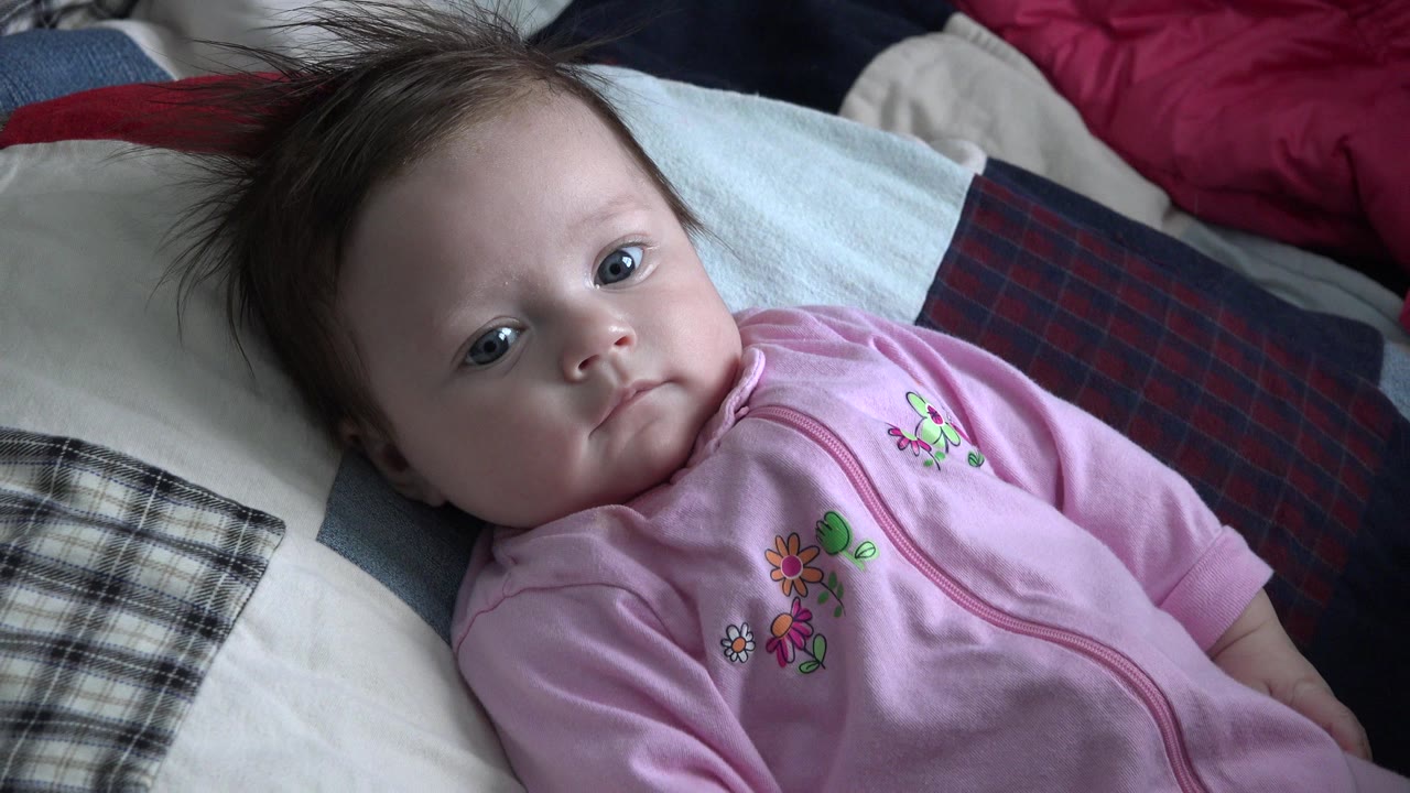 Baby in a pink outfit lying on pillows and blankets.