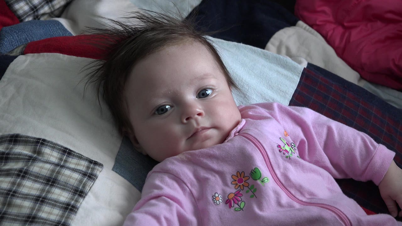 Baby in pink pajamas lying on cushions