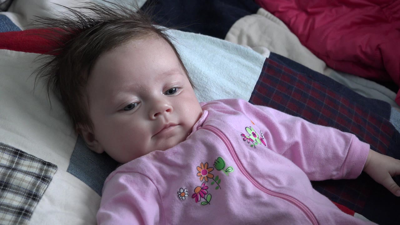 Baby lying on blankets in a pink outfit.